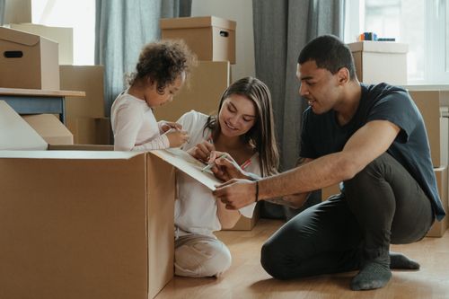 Famille avec deux enfants et un déménageur examinant le plan des cartons, dans une pièce remplie de boîtes.